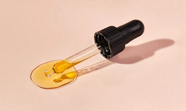 A dropper releasing yellow liquid on a surface