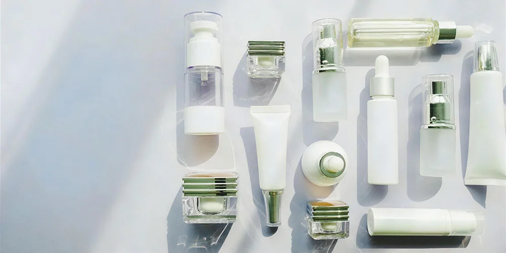 Various cosmetic products and containers, including pumps, tubes, and bottles, arranged in a flatlay on a light surface.
