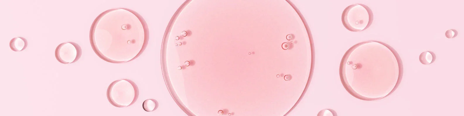 Pink liquid bubbles varying in size on a pale pink background, creating an abstract and serene pattern.