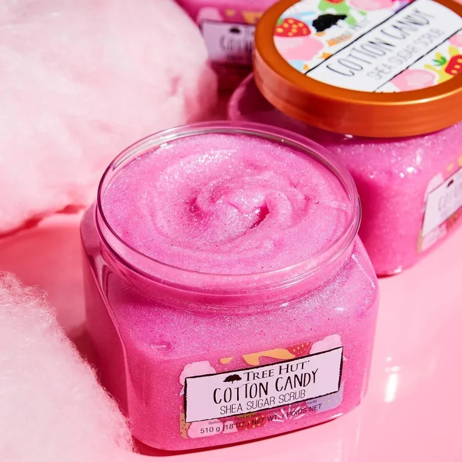 Lulur shea gula rasa permen kapas Tree Hut dalam wadah merah muda dengan hiasan permen kapas di permukaan merah muda.