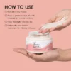 Hands holding Xiran exfoliating body scrub jar with product instructions displayed on pink background.
