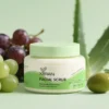 Xiran facial scrub in a jar with green lid, surrounded by grapes and aloe, highlighting natural ingredients.
