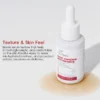 Xiran Post-Procedure Restore Serum bottle on a pale surface with brown serum spill, highlighting smooth texture and skin benefits.