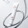 Tube of post-procedure scab-softening cream placed against a minimalist background with intertwining metallic elements.