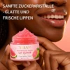 A close-up of a smiling woman holding a jar of watermelon and guava lip scrub with pink sugar crystals, showing smooth and glossy lips.