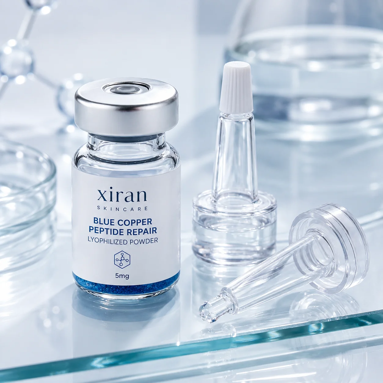 Un flacon en verre étiqueté « Poudre lyophilisée réparatrice aux peptides de cuivre bleu Xiran Skincare » entouré d'applicateurs transparents sur une surface réfléchissante.