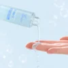 Close-up of a clear hydrating serum being poured from a bottle with blue packaging onto fingers, set against a light blue background.