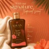 Xiran Sun Glow Oil tanning product in a brown bottle with gold cap, on beige fabric and an orange background with tropical floral accents.