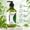 Green bottle of tea tree oil anti-dandruff shampoo on a marble surface with fresh leaves and product attributes, highlighting no parabens, mineral oil, artificial colors, or petroleum.