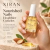 A hand holding a bottle of Xiran Skincare Nail & Cuticle Oil, surrounded by almonds, oil drops, and green leaves on a beige background.